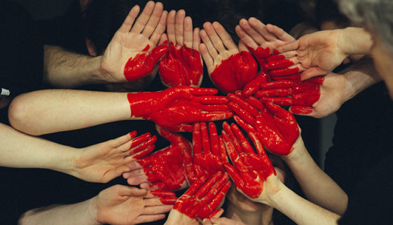 Mãos pintadas de vermelho se juntam para formar um coração.