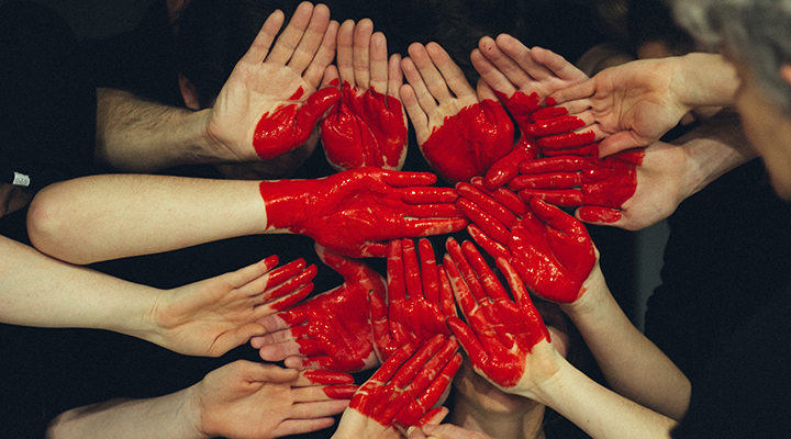 Mãos pintadas de vermelho se juntam para formar um coração.