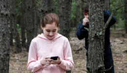 A maniac watches from behind a tree in the forest for a teenage girl in a tracksuit with a mobile phone in her hands. The concept of child abduction.