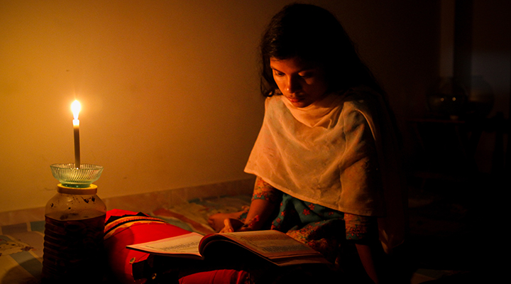 A young girl studying at home with candlelight after electricity