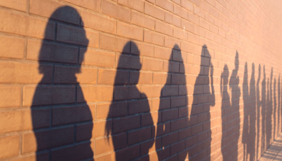 a line of shadows of people lined up against a red brick wall. Stand in a queue to the changes