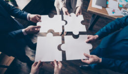 Cropped top above high angle view of stylish elegant sharks holding in hands fitting big large puzzle pieces together team building in loft industrial interior work place station