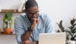 Head shot serious puzzled African American businessman looking at laptop