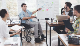 Office workers and man in a wheelchair discussing business moments in a modern office.