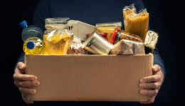 A man holding a donation box of different products on dark background