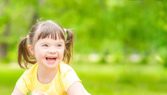Portrait of a joyful little girl with syndrome down in a summer