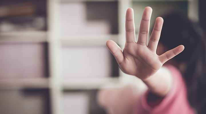 Foto com tirada com foco em primeiro plano da mão aberta de uma criança. A criança sinaliza o "pare" enquanto aparece ao fundo se virando de costas.