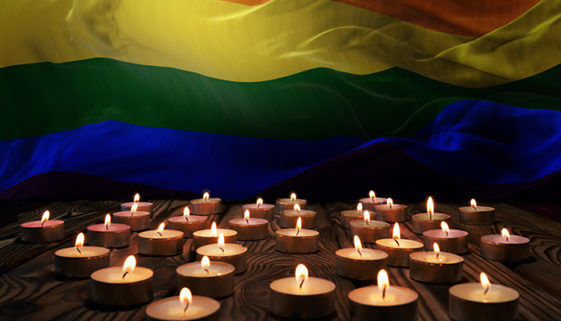 Pequenas velas de luto queimando e a bandeira nacional LGBTI  ao fundo.