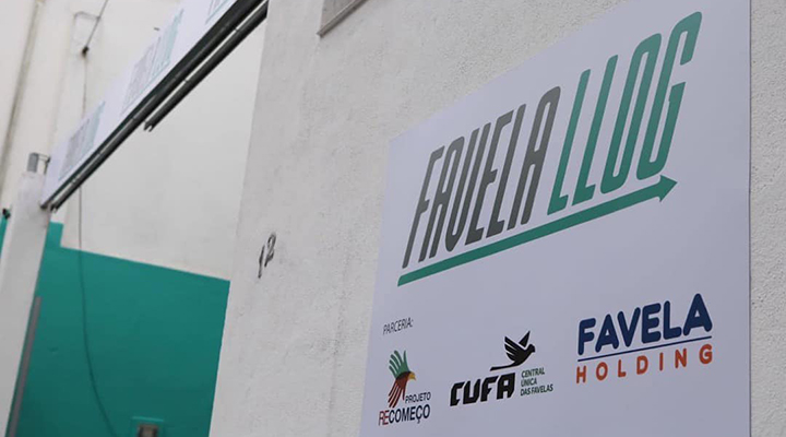 Foto tirada da placa de fundo branco que leva o nome Favela (em preto) Llog (em verde) sublinhada com uma seta, em direção à direito, também verde. Abaixo estão os logos do Projeto Recomeço, da CUFA e da Favela Holding.