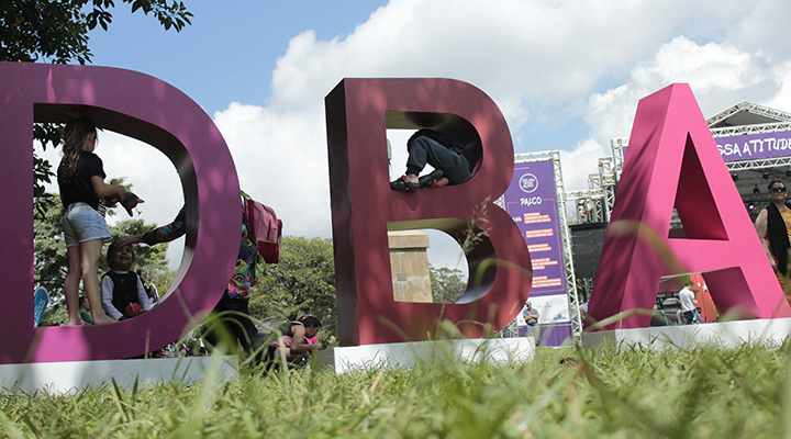 Foto das letras D, B e A postas em um gramado. Está de dia e pessoas interagem com as letras. | São Paulo receberá a 7ª edição do Dia das Boas Ações
