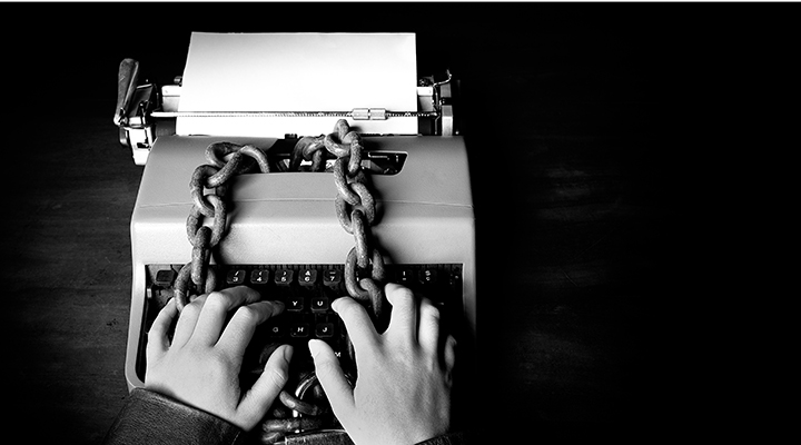 Mãos escrevendo em uma máquina de escrever trancada com uma corrente. | Brasil está em 110º no Ranking Mundial de Liberdade de Imprensa