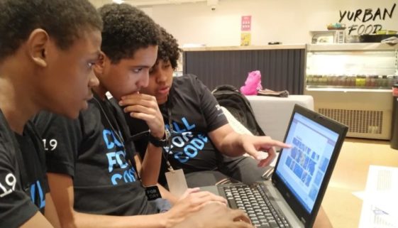 Foto de três jovens negros interagindo com a tela de um notebook.