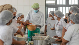 Foto de alunas no curso de Gastronomia Social tomando aula com professor em volta de uma mesa com várias panelas e utensílios.