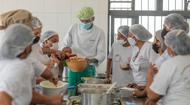 Foto de alunas no curso de Gastronomia Social tomando aula com professor em volta de uma mesa com várias panelas e utensílios.