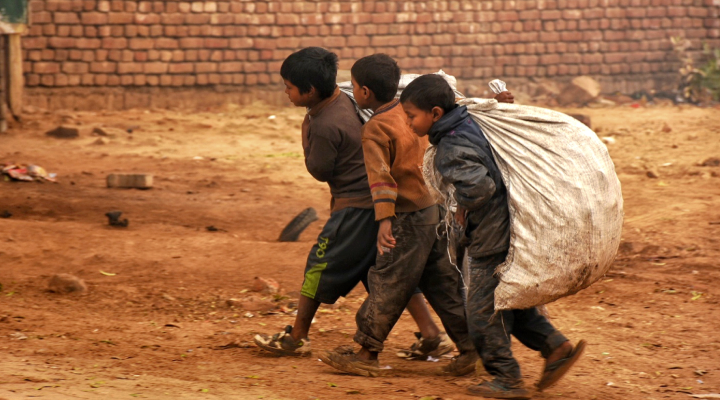 Crianças andam em chão de terra carregando saco branco