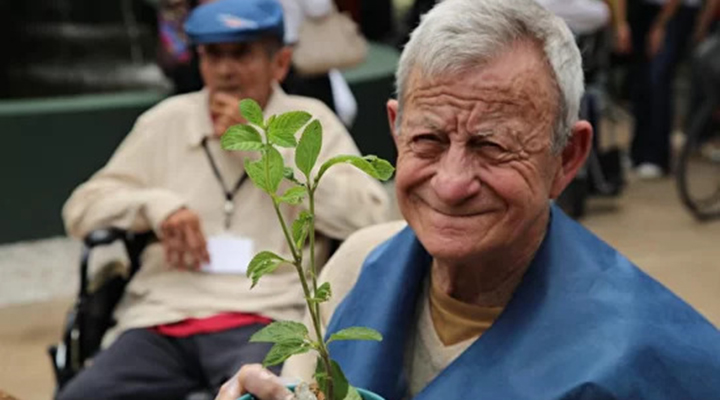 Foto de um senhor sorrindo e segurando uma planta.