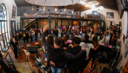 Foto panorâmica de pessoas reunidas em salão iluminado pela luz do dia., se abraçando e comemorando.