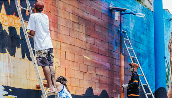 Foto de três pessoas pintando um muro alto.