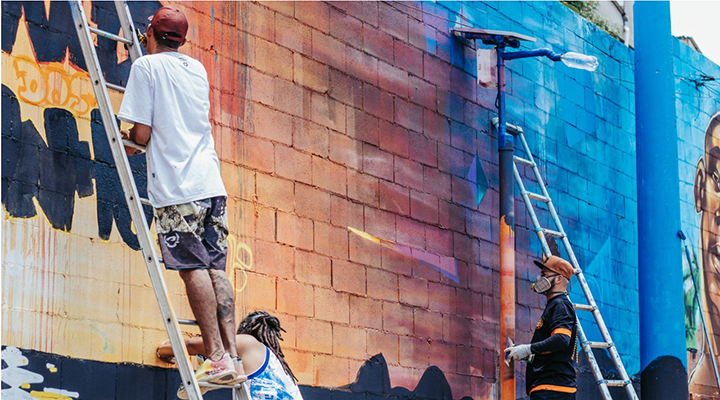 Foto de três pessoas pintando um muro alto.