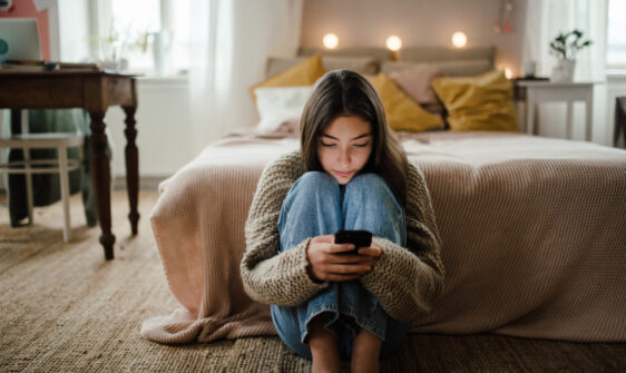Teenage girl sitting on the floor and scrolling her smartphone.