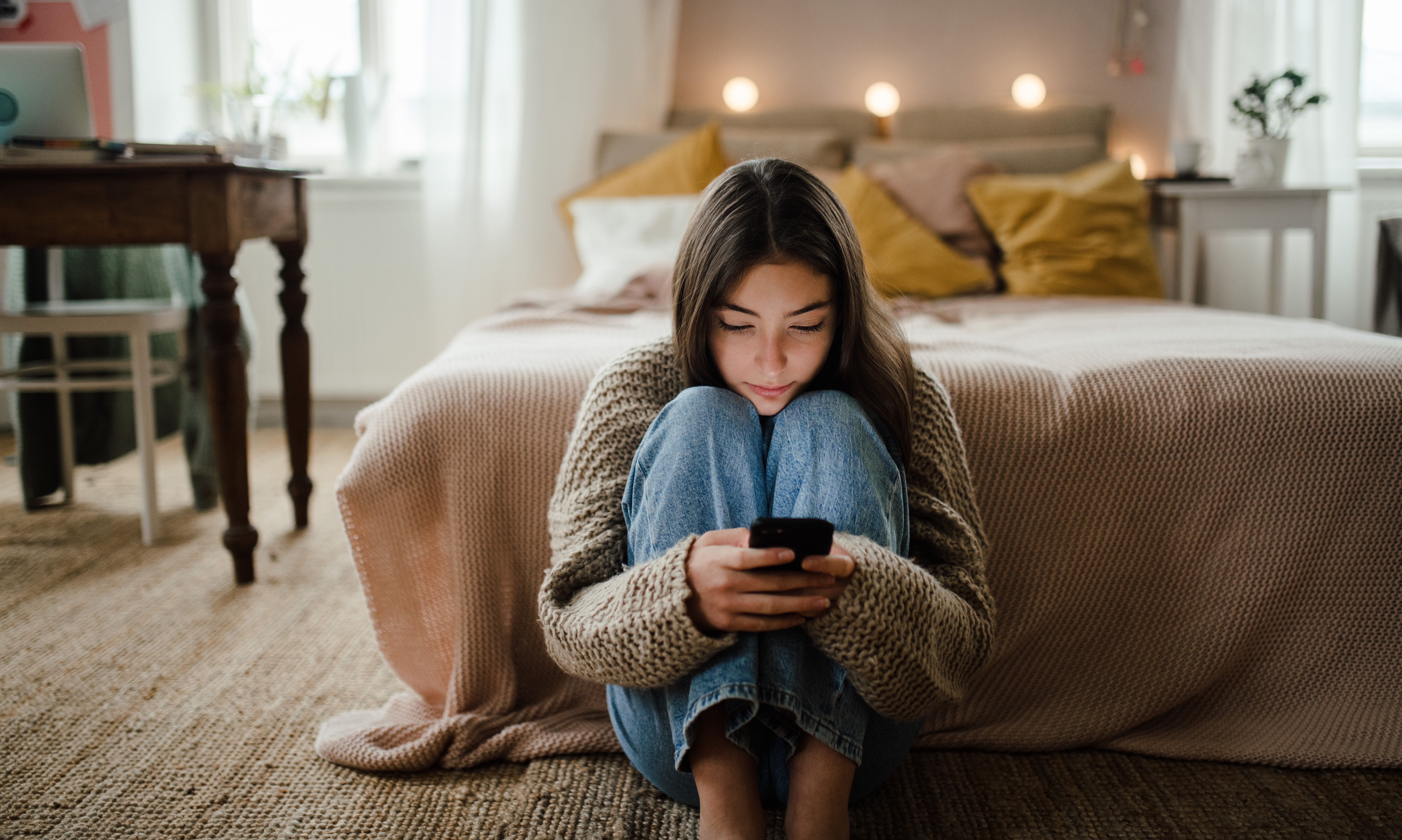 Teenage girl sitting on the floor and scrolling her smartphone.