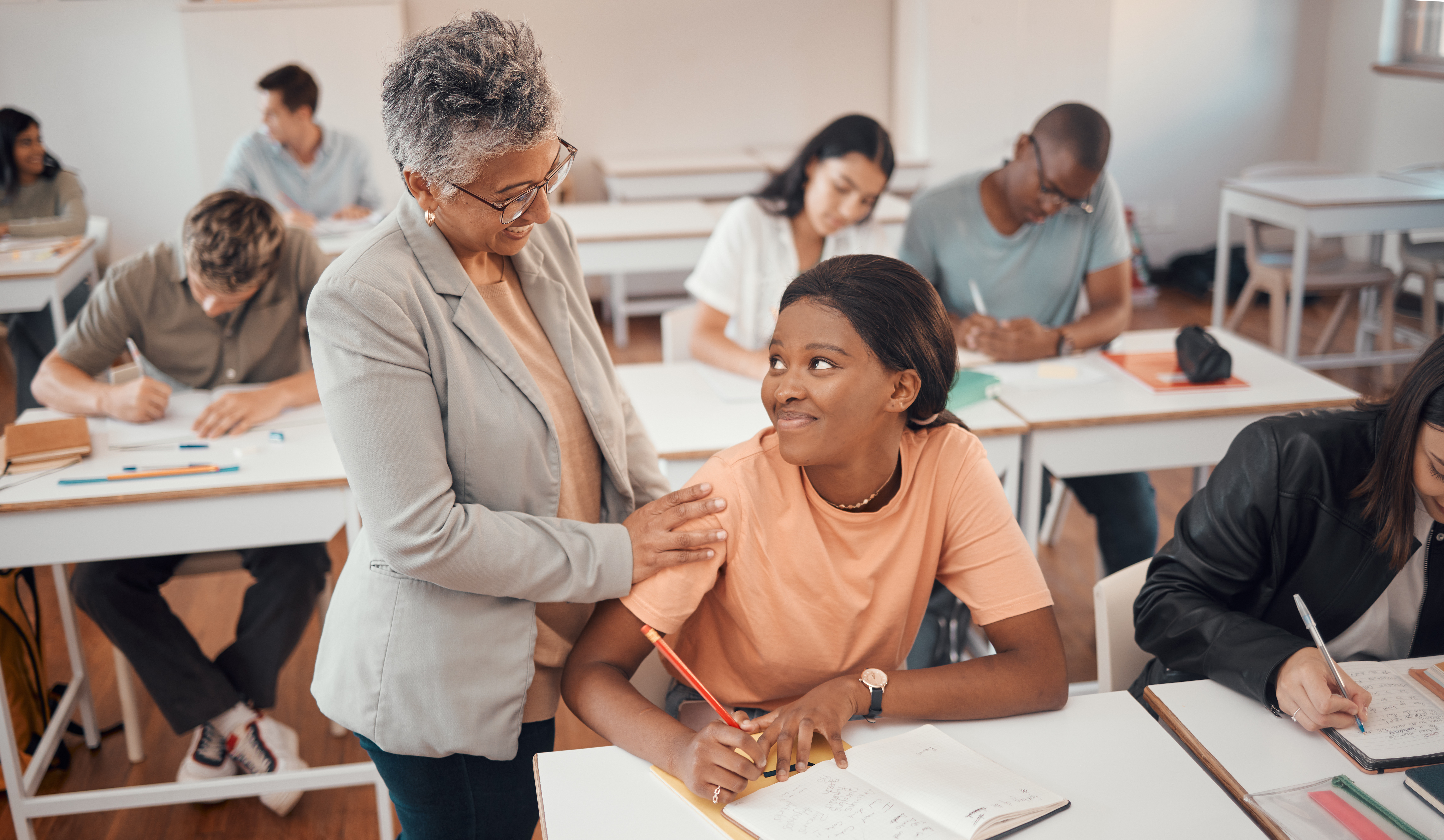 Professora da apoio a aluna colocando a mão no ombro, ambas são mulhere negras 