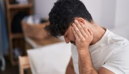 Young hispanic man suffering for backache sitting on bed at bedroom
