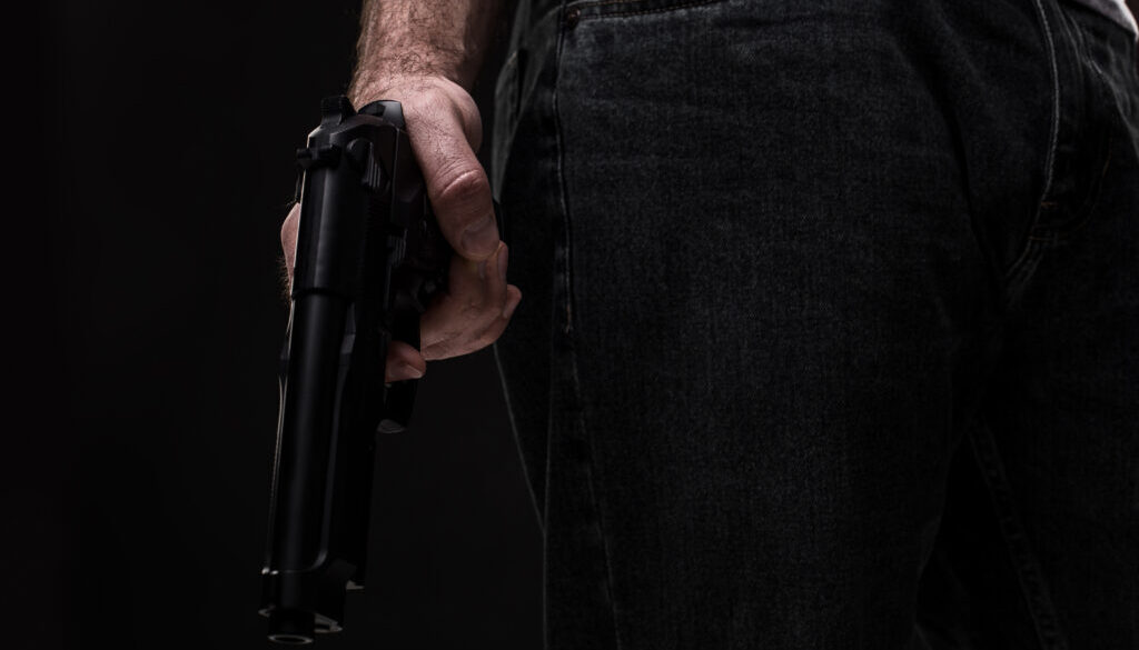 Killer with gun on black background at the studio
