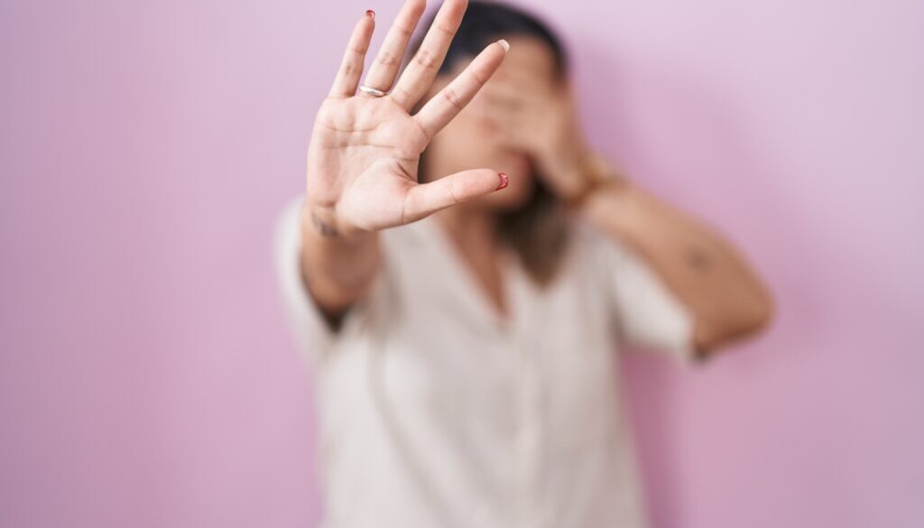 Blonde woman standing over pink background covering eyes with hands and doing stop gesture with sad and fear expression. embarrassed and negative concept.