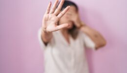 Blonde woman standing over pink background covering eyes with hands and doing stop gesture with sad and fear expression. embarrassed and negative concept.